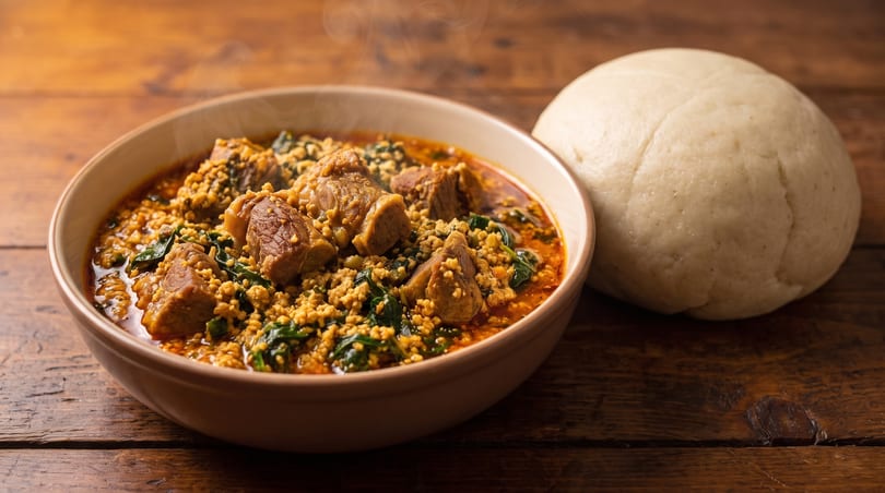 Steaming bowl of Nigerian Egusi soup with meat and greens, served with a side of pounded yam.