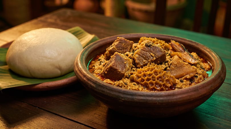 A bowl of Nigerian Egusi soup with beef and tripe, served with pounded yam on a banana leaf.